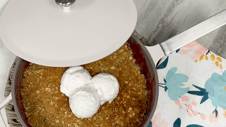 Berry Crumble made inside of the gray pan topped off with vanilla ice-cream on a marble background