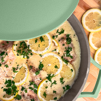 Lemon Garlic Chicken inside of The Pan in Green on a cutting board with garnish and lemon
