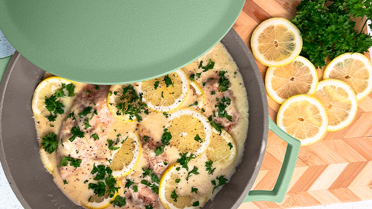 Lemon Garlic Chicken inside of The Pan in Green on a cutting board with garnish and lemon