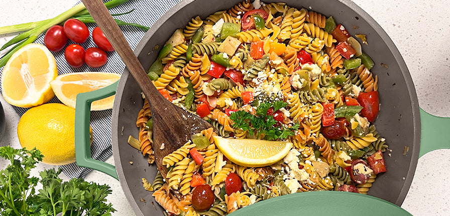 Pasta cooked in the pan with tomatoes and olives surrounded by lemons and other garnish