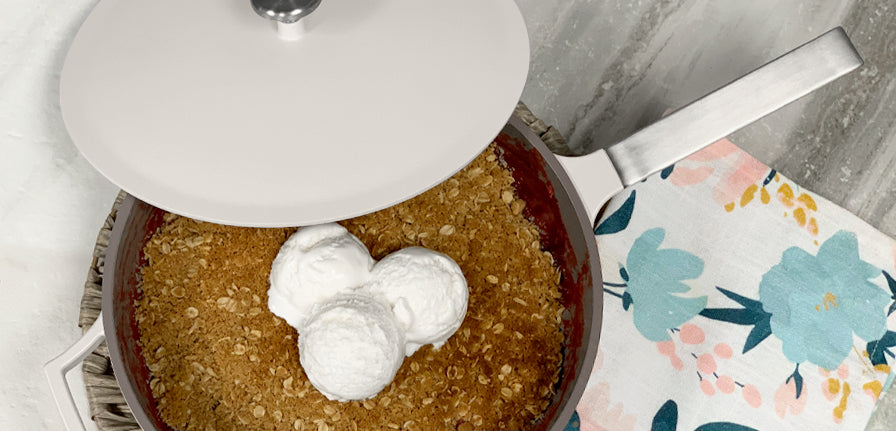 Berry Crumble made inside of the gray pan topped off with vanilla ice-cream on a marble background