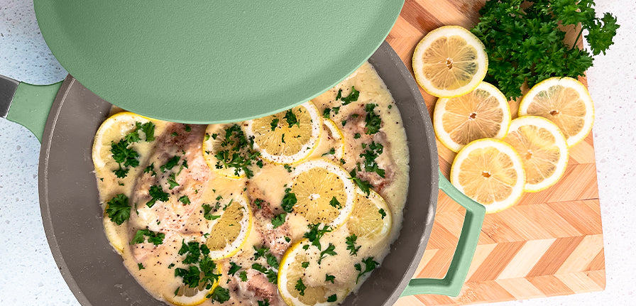 Lemon Garlic Chicken inside of The Pan in Green on a cutting board with garnish and lemon