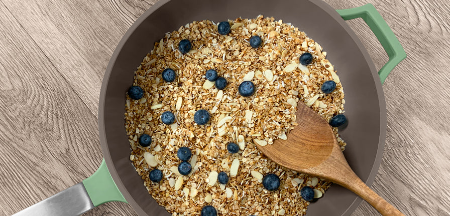 Skillet Granola inside of The Pan in Green topped with blueberries on a wood texture